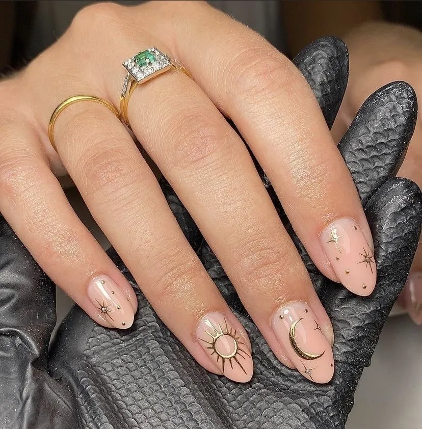 Uñas nude con diseño celestial en dorado: sol, luna y estrellas